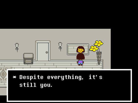 Pixel art video game screenshot of a small character with brown hair, a dark top and a striped shirt standing in a gray hallway with a door, wall lamps, a chair and a vase of yellow flowers. A dialogue box reads: "* Despite everything, it's still you."
