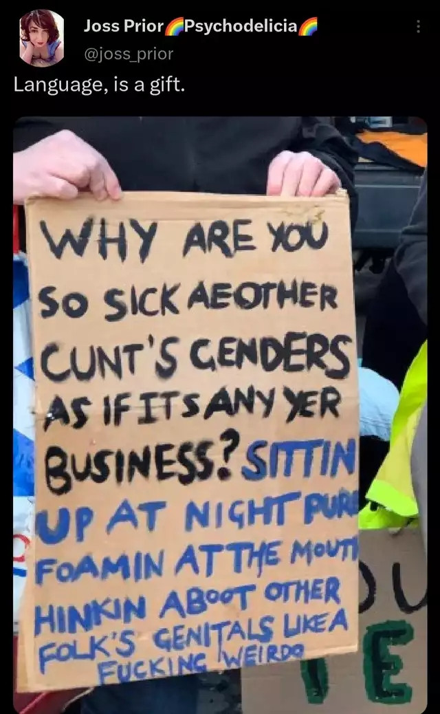 Screenshot of a post by Joss Prior (@joss_prior) reading "Language, is a gift." Below it, a person holds a cardboard protest sign. Black paint reads: "WHY ARE YOU SO SICK AE OTHER CUNT'S GENDERS AS IF ITS ANY YER BUSINESS?" Blue paint continues: "SITTIN UP AT NIGHT PURE FOAMIN AT THE MOUTH HINKIN ABOOT OTHER FOLK'S GENITALS LIKE A FUCKING WEIRDO"