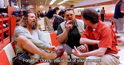 Movie still in a bowling alley: a long-haired bearded man in a gray cardigan sits with his foot up, a heavy man in tinted glasses and a vest holds a cigarette, and a younger man in an orange shirt listens. Caption: "Forget it, Donny, you're out of your element!"