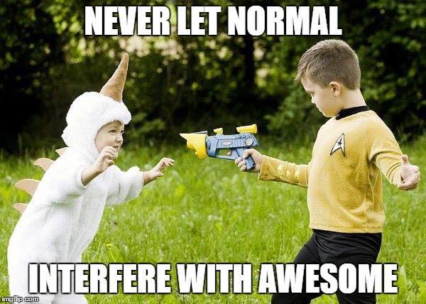 A small child in a white unicorn costume with a horn and spines crouches with arms out on a grassy lawn, facing a boy in a yellow Star Trek command uniform who points a toy blue and yellow space blaster at them. Top text: "NEVER LET NORMAL". Bottom text: "INTERFERE WITH AWESOME".
