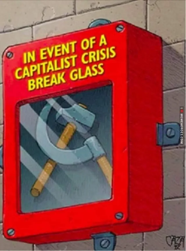 Cartoon illustration of a red emergency box mounted on a brick wall, like a fire alarm. Yellow text on top reads "IN EVENT OF A CAPITALIST CRISIS BREAK GLASS". Behind the glass pane is a hammer and sickle. A watermark on the right reads "I MEMEHEROES.COM".
