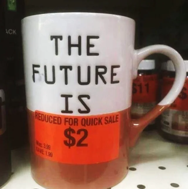 A white and brown ceramic mug on a store shelf. Black block letters on the mug read "THE FUTURE IS". A red-orange clearance sticker over the brown part reads "REDUCED FOR QUICK SALE $2", with small print "Was: 3.99 Save: 1.99".