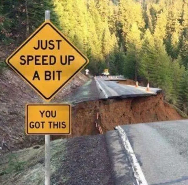 Photo of a mountain road that has collapsed into a huge gap, with a raised broken slab of asphalt on the far side. A yellow diamond road sign reads "JUST SPEED UP A BIT". A smaller yellow sign below it reads "YOU GOT THIS". Evergreen forest in the background.
