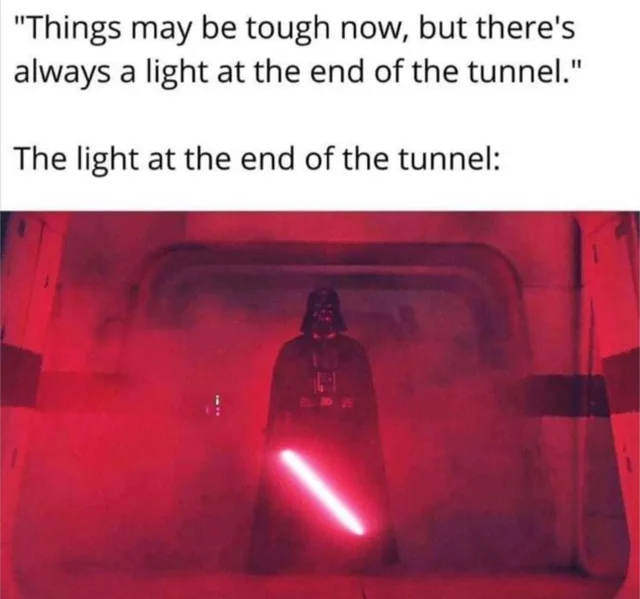 Top text on a white background reads: "Things may be tough now, but there's always a light at the end of the tunnel." Below, the text reads: "The light at the end of the tunnel:" The photo shows a caped figure in a black helmet, Darth Vader, in a red-lit corridor holding a glowing red lightsaber.