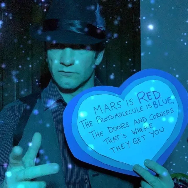 A man in a dark fedora, eyes shadowed, lit in blue with glowing sparkles, holds a blue paper heart. Handwritten on it: "Mars is red, the Protomolecule is blue, the doors and corners that's where they get you."