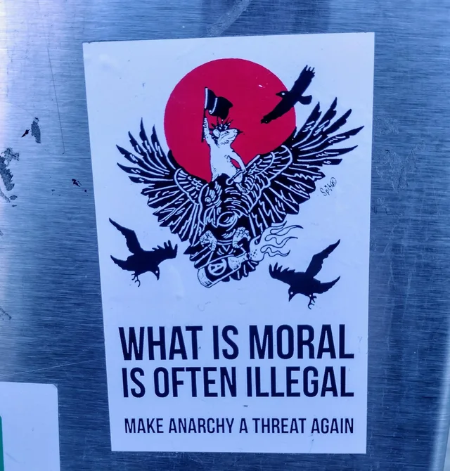 Sticker on brushed metal showing a white rat with a spiked collar holding a black flag, riding a black winged creature in front of a red sun, with three black crows flying around. Text: "WHAT IS MORAL IS OFTEN ILLEGAL" and "MAKE ANARCHY A THREAT AGAIN".