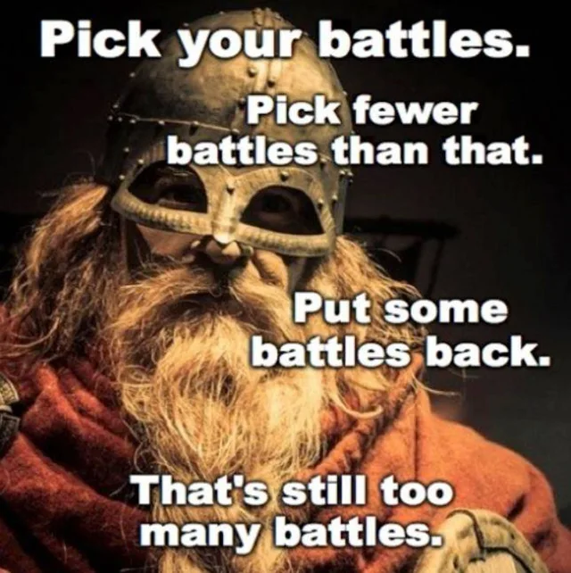 A bearded warrior in a riveted metal helmet with a eyeguard mask and a rust-orange wool cloak, lit warmly against a dark background. Text: "Pick your battles. Pick fewer battles than that. Put some battles back. That's still too many battles."
