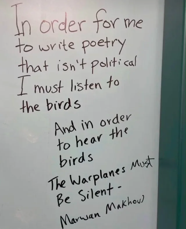 Handwritten black marker poem on a whiteboard: "In order for me to write poetry that isn't political I must listen to the birds. And in order to hear the birds The Warplanes Must Be Silent - Marwan Makhoul"