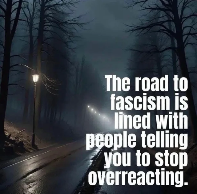 A dark, foggy road at night, lined with bare trees and a lit street lamp, with distant lights fading into mist. White text reads: "The road to fascism is lined with people telling you to stop overreacting."