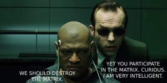 Movie still of a bald man with an earpiece wire, a bruised face and a stern look, with a man in dark sunglasses and a suit leaning in behind him. Caption on the bald man: "WE SHOULD DESTROY THE MATRIX." Caption on the other man: "YET YOU PARTICIPATE IN THE MATRIX. CURIOUS. I AM VERY INTELLIGENT."